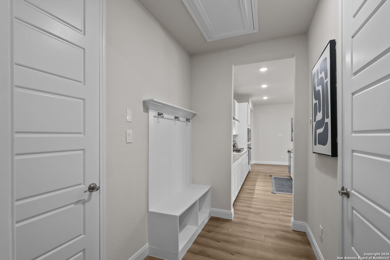 Modern entryway with built-in white coat rack, bench, and open kitchen view in Davidson Homes The Lanier H, Ladera, San Antonio
