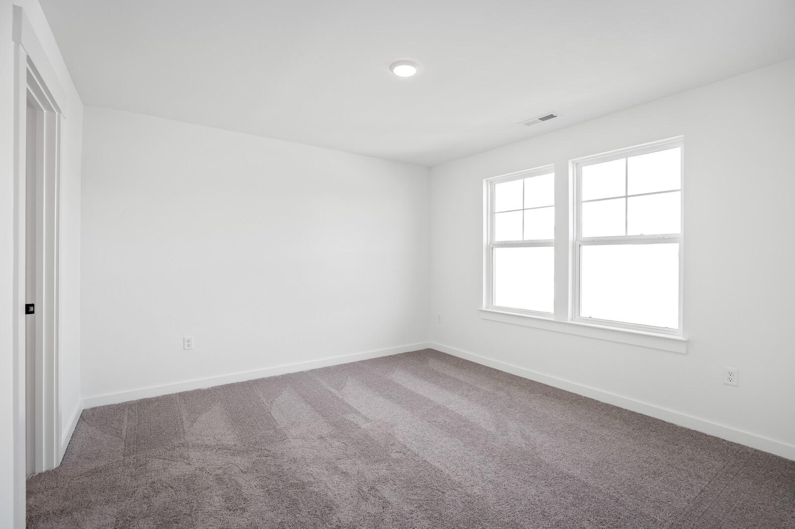 Bright empty bedroom with white walls, double windows, and gray carpet in Davidson Homes The Willow, Gallatin TN