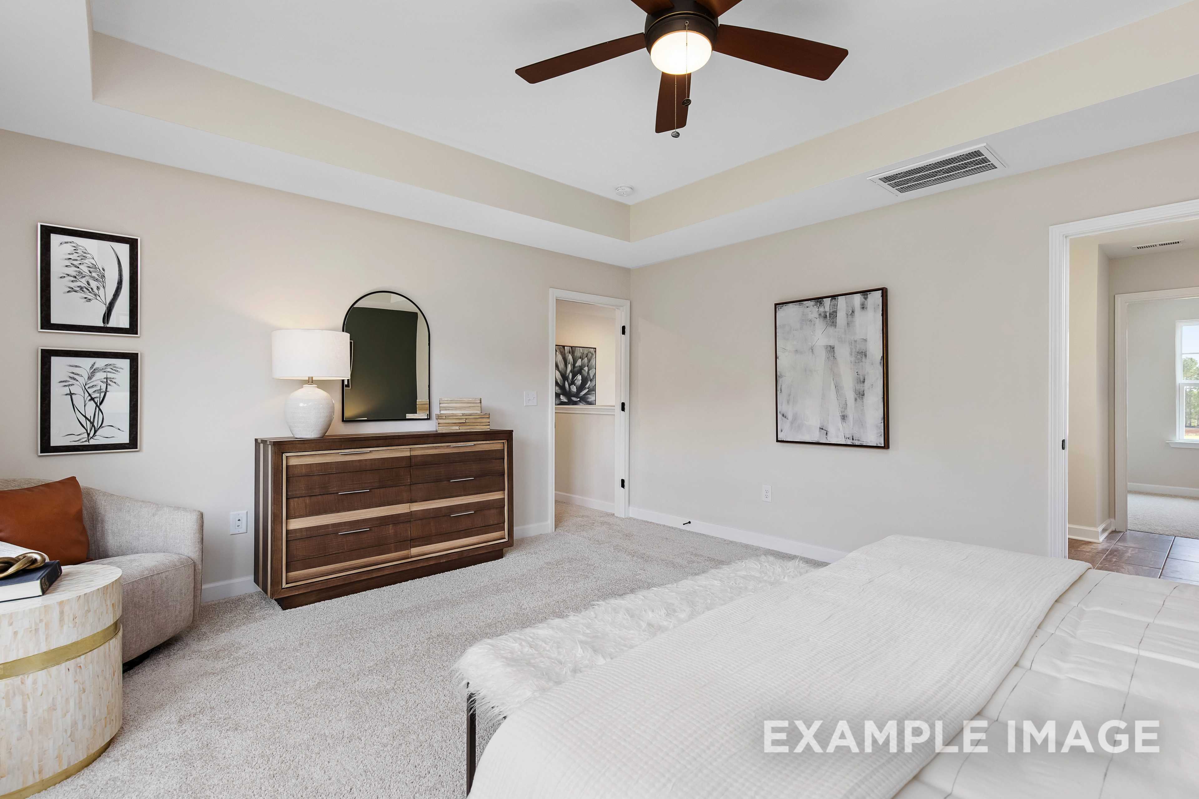 Spacious master bedroom in The Willow B with king bed, wooden dresser, arched mirror, and neutral tones