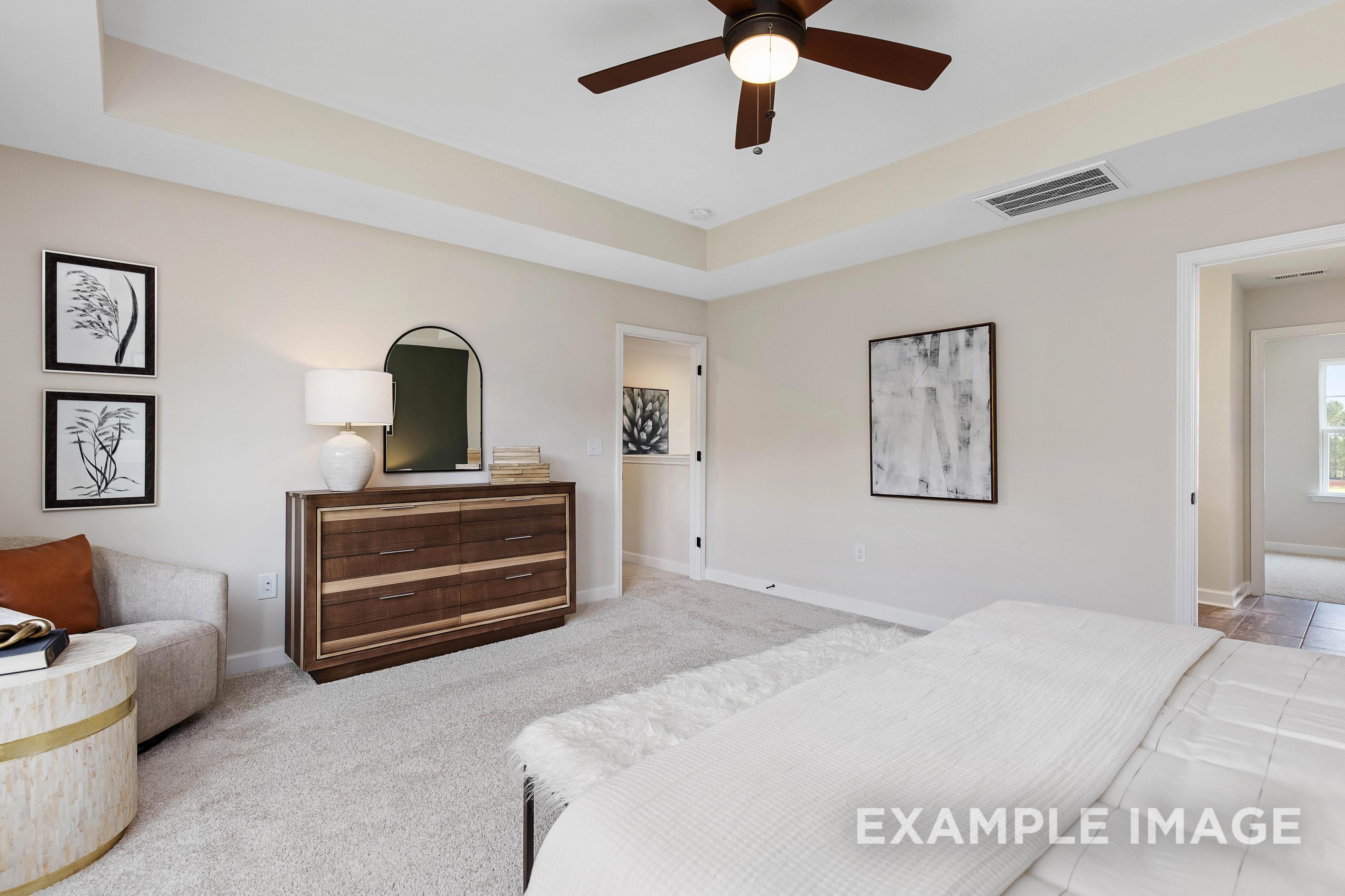 Spacious master bedroom in The Willow B with king bed, wooden dresser, arched mirror, and neutral tones
