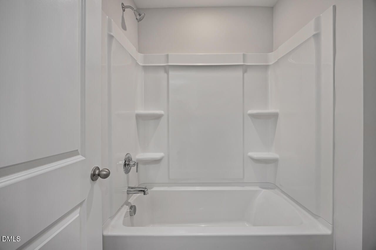 White bathtub and shower combo with built-in shelving in a Davidson Homes Mitchell floor plan at Camden Park, Knightdale.