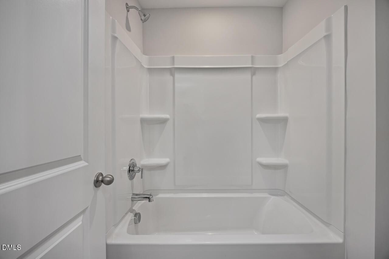 White bathtub and shower combo with built-in shelving in a Davidson Homes Mitchell floor plan at Camden Park, Knightdale.
