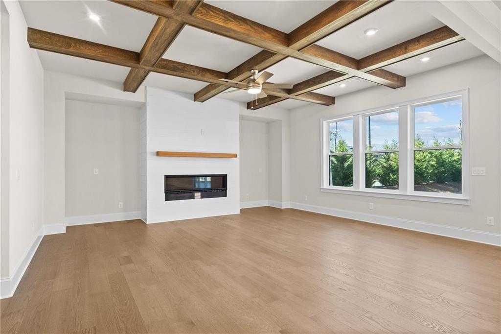 Spacious living room with coffered wooden beams, white fireplace, ceiling fan, and large windows in Davidson Homes The Arlington A, East Cobb