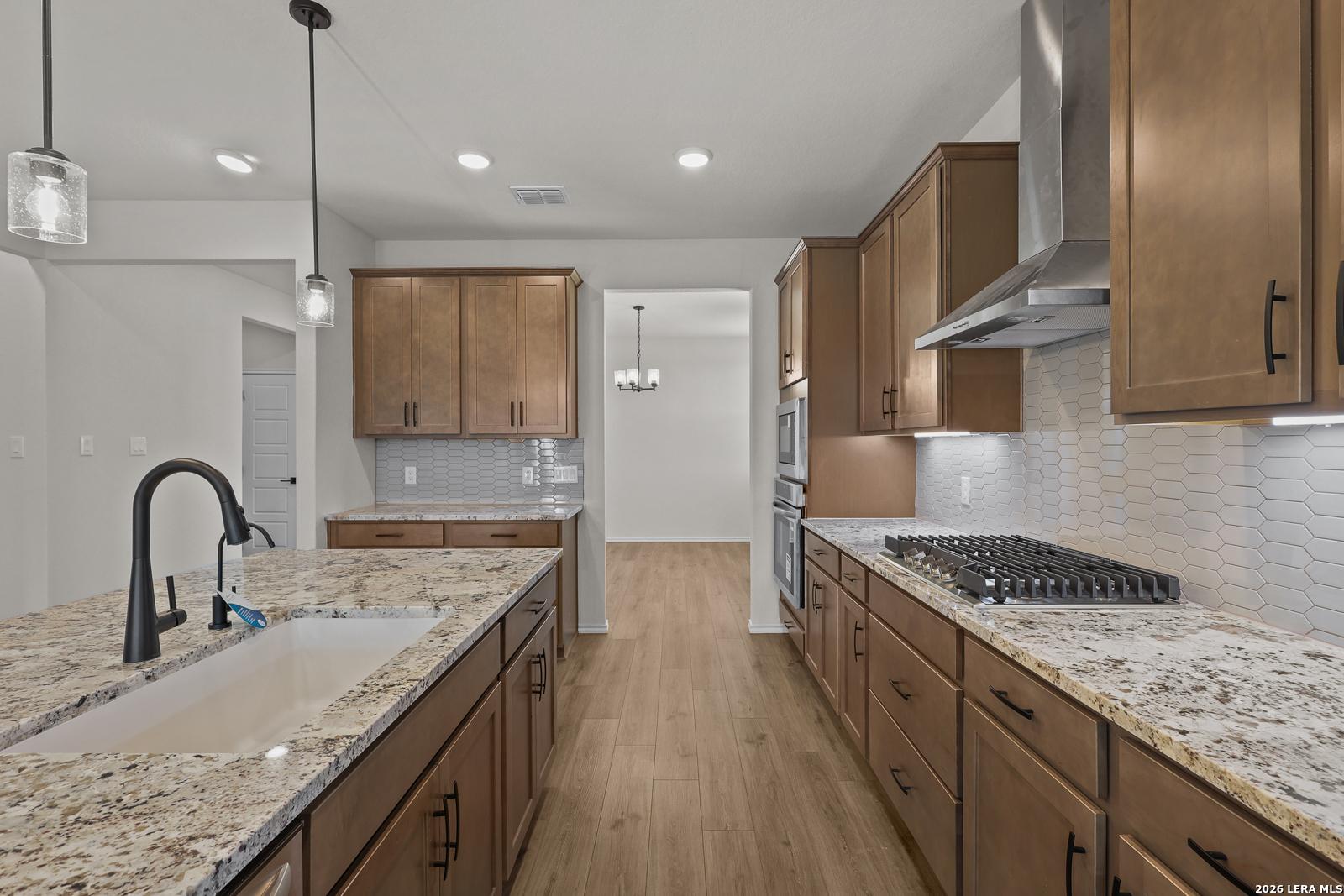 Modern kitchen with granite island, hexagon tile backsplash, and gas cooktop in The Glenwood E by Davidson Homes, San Antonio