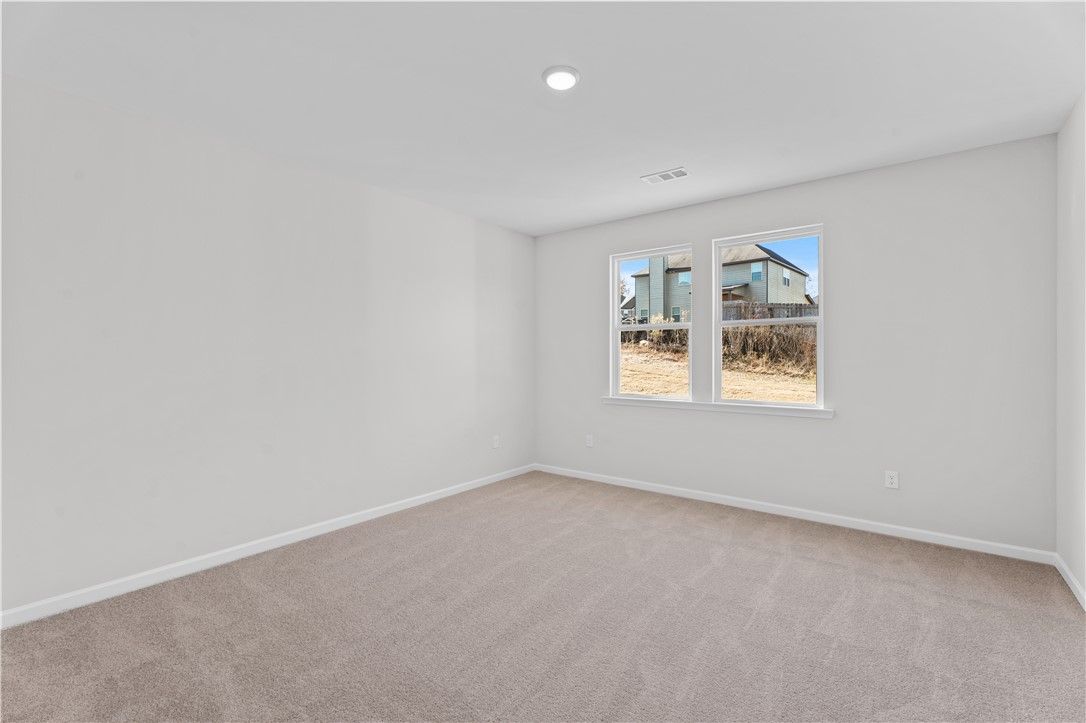Bright empty bedroom with light gray walls, beige carpet, and windows overlooking neighborhood in Davidson Homes The Luna B, Opelika, Alabama