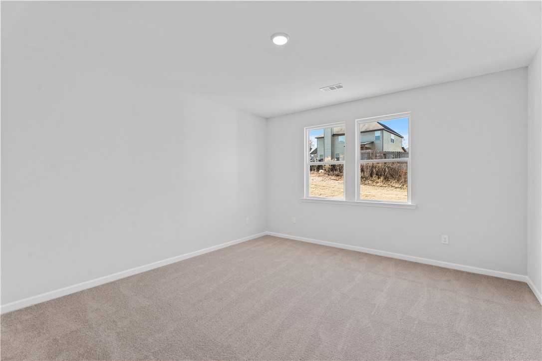 Bright empty bedroom with light gray walls, beige carpet, and windows overlooking neighborhood in Davidson Homes The Luna B, Opelika, Alabama