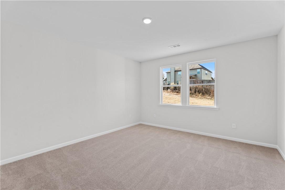 Bright empty bedroom with light gray walls, beige carpet, and windows overlooking neighborhood in Davidson Homes The Luna B, Opelika, Alabama