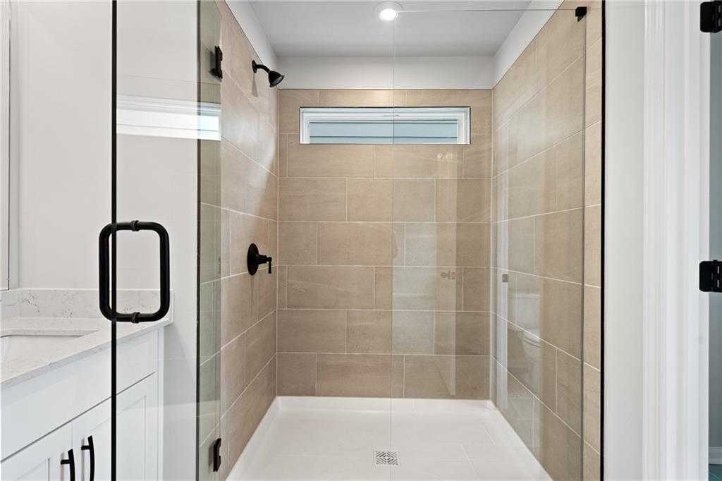 Modern frameless glass shower with beige tile walls, rainfall showerhead, and adjacent vanity in Davidson Homes The Marion A, Kennesaw, GA