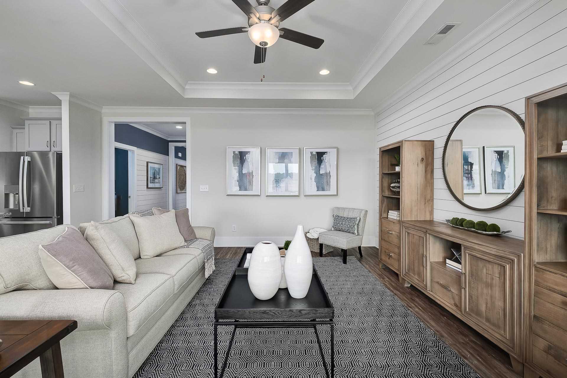 Cozy living room in The Everett C home with beige sofa, wooden built-ins, abstract art, shiplap walls, and open kitchen view