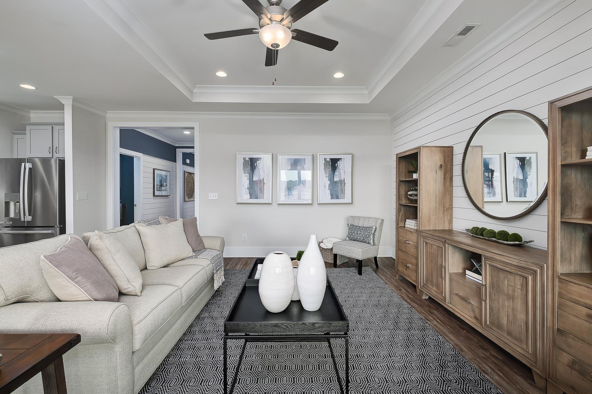 Cozy living room in The Everett by Davidson Homes featuring cream sectional sofa, abstract art, wooden bookshelves, and ceiling fan