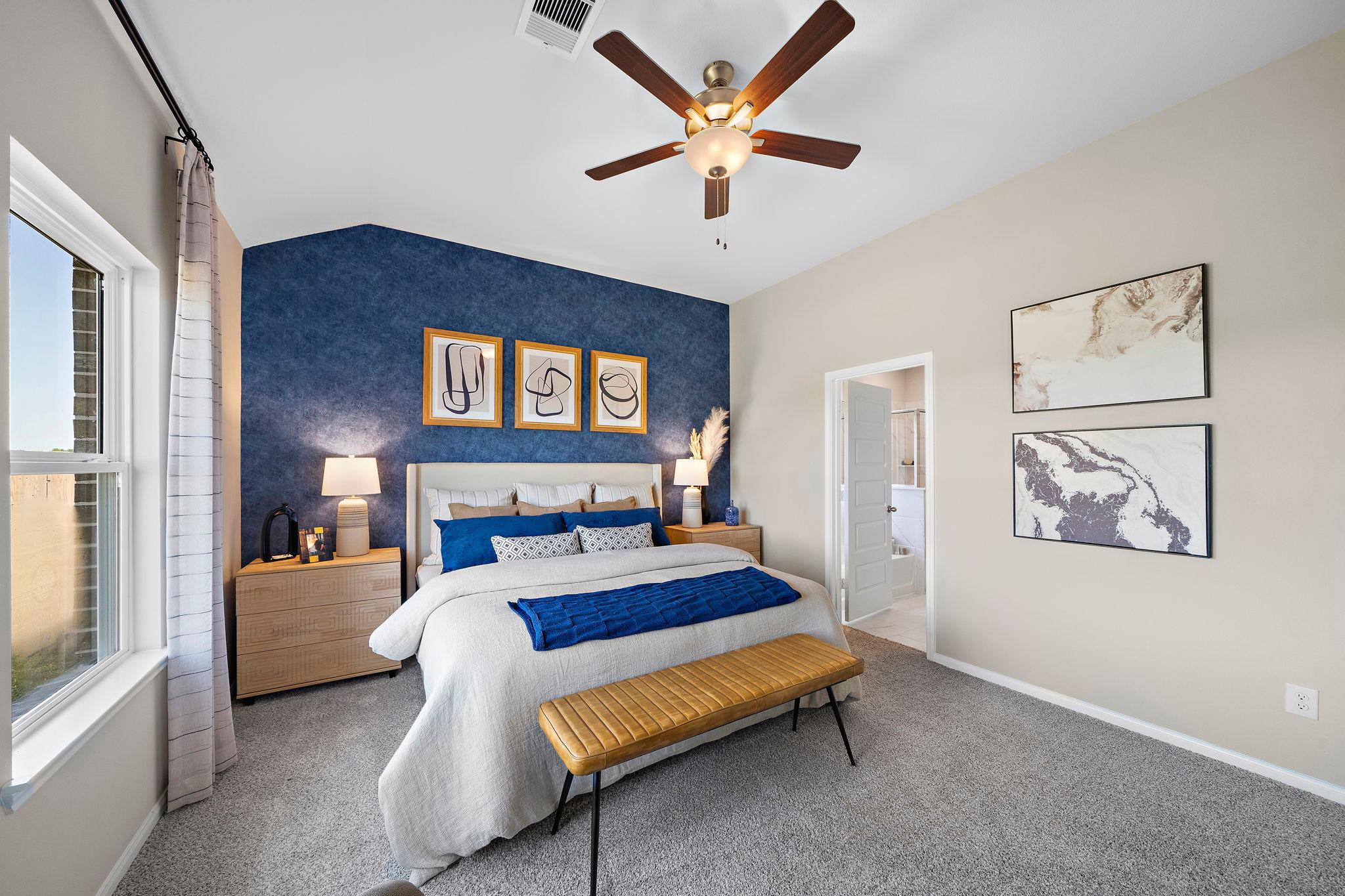 Spacious master bedroom at Emberly in Beasley Texas by Davidson Homes with blue accent wall, king bed, abstract art, and ceiling fan