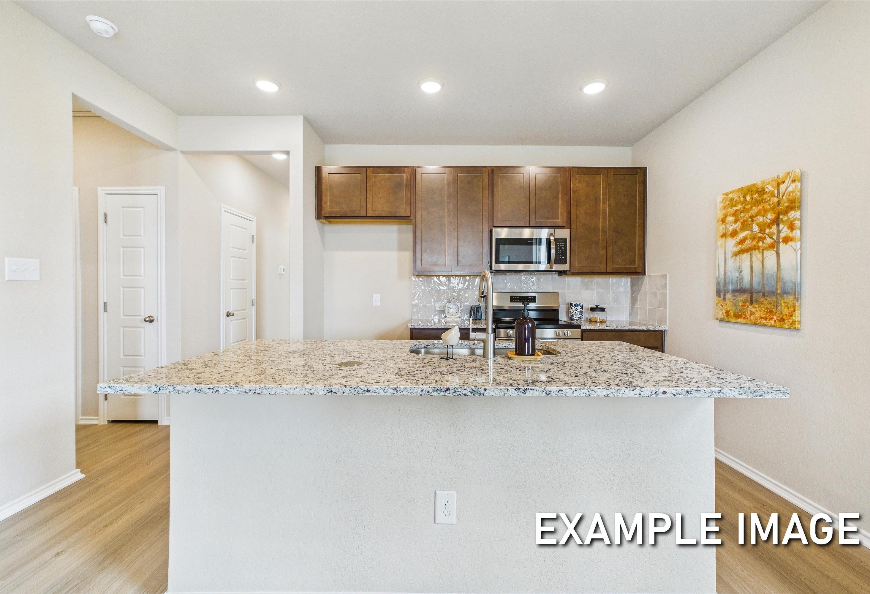 Modern kitchen in The Corral featuring a granite island, dark wood cabinetry, and stainless steel appliances.