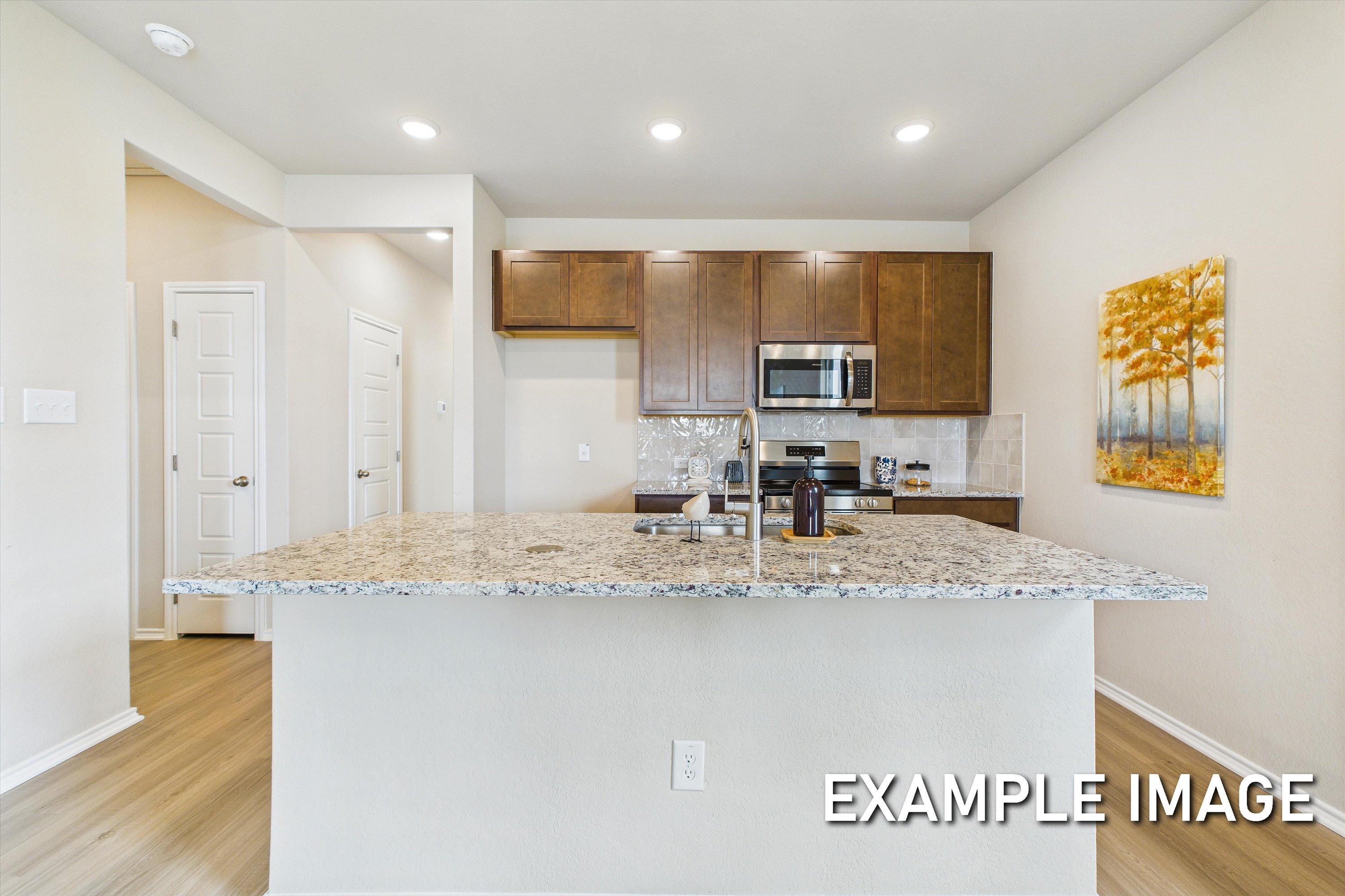 Modern kitchen in The Comal by Davidson Homes featuring granite island, dark wood cabinets, and stainless steel appliances.