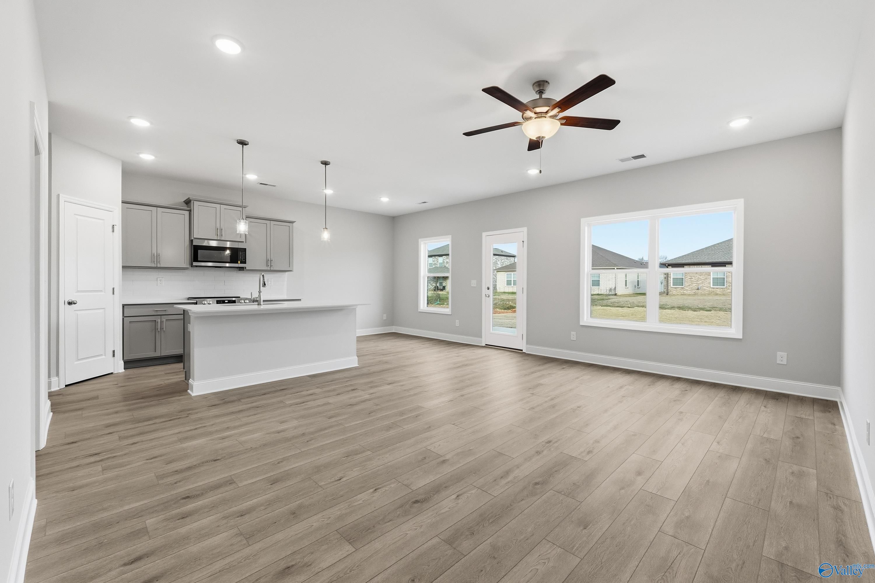 Modern open kitchen-living area with gray cabinets, white island, hardwood floors, ceiling fan in Davidson Homes The Butler, Toney, Alabama