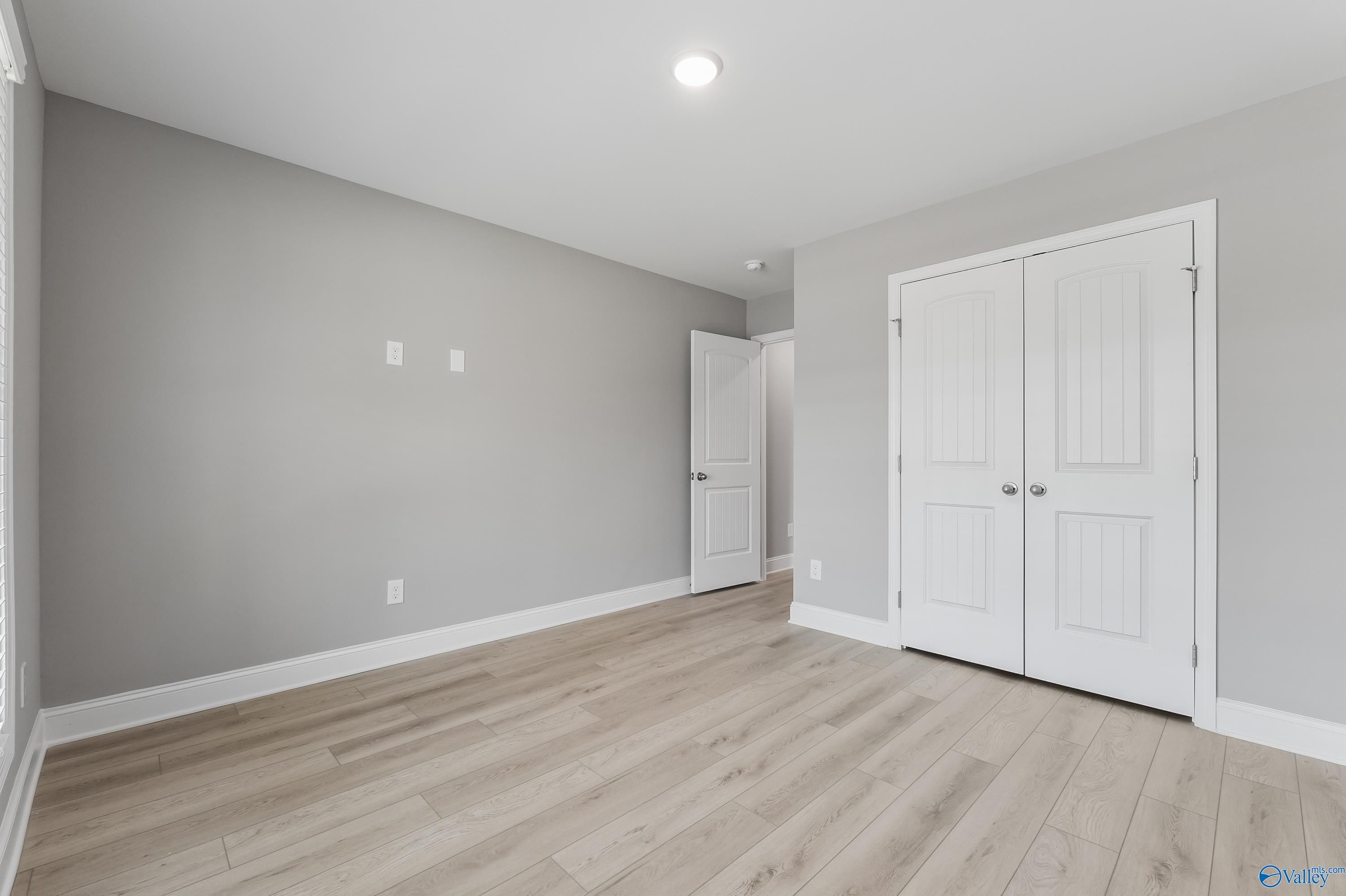 Spacious bedroom with light gray walls, hardwood floors, and double closet doors in Davidson Homes The Everett B, Athens, Alabama