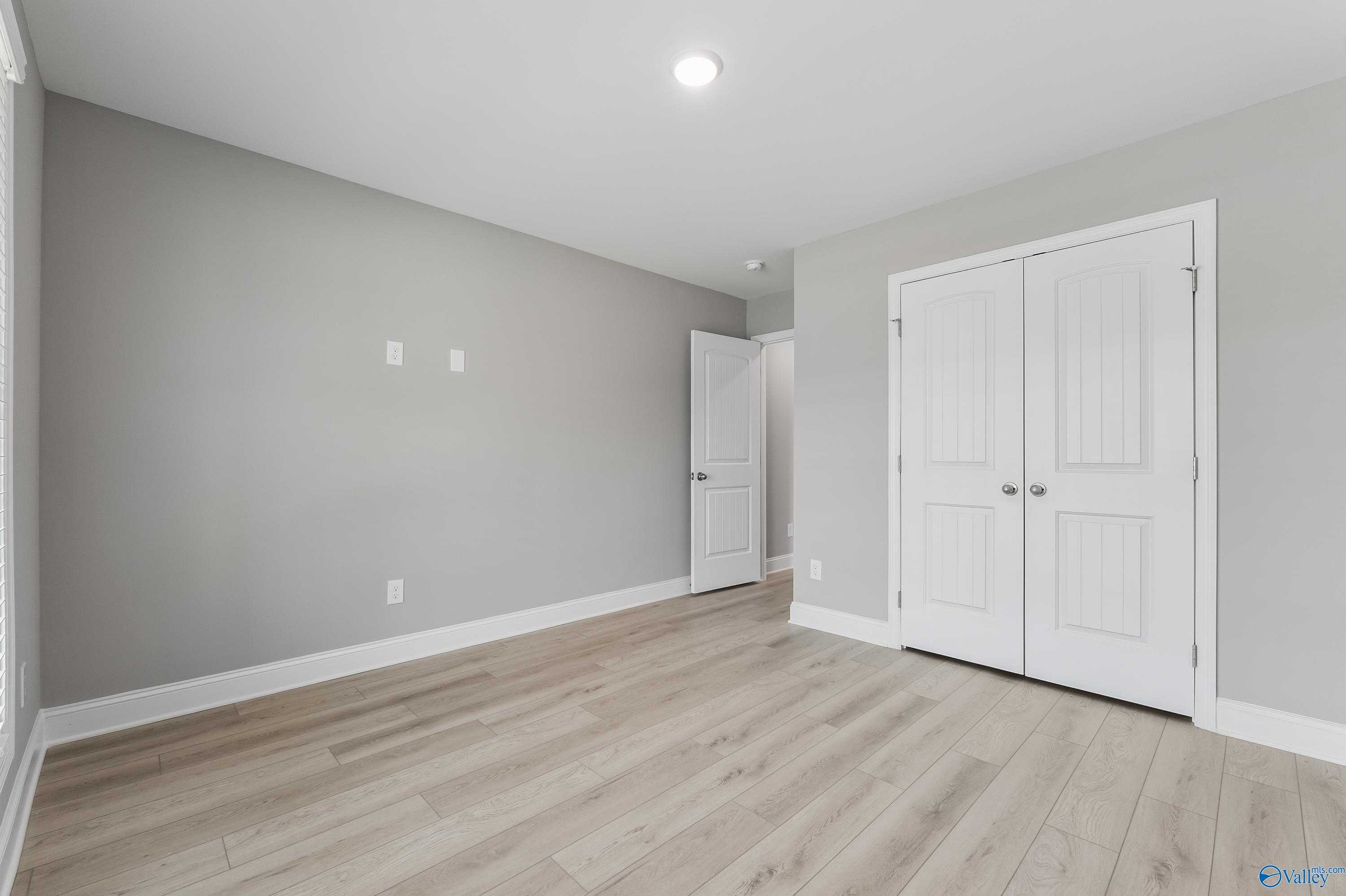 Spacious empty bedroom with light gray walls, hardwood floors, and white double closet doors in Davidson Homes The Everett B, Athens AL
