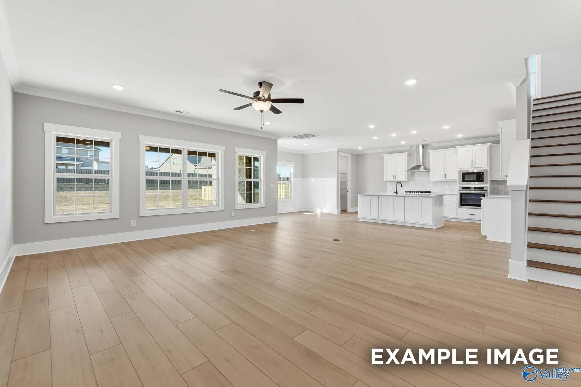 Open-concept living room and kitchen with light wood floors, white cabinets, large windows, and ceiling fan in The Emory floor plan, Decatur, AL