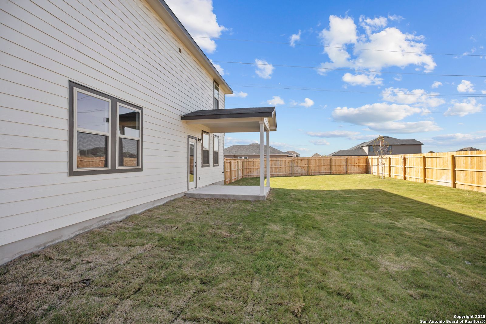 Side view of 2-story white home with covered entry, large windows, and fenced grassy backyard in Hannah Heights, Seguin, Texas - Davidson Homes Douglas C