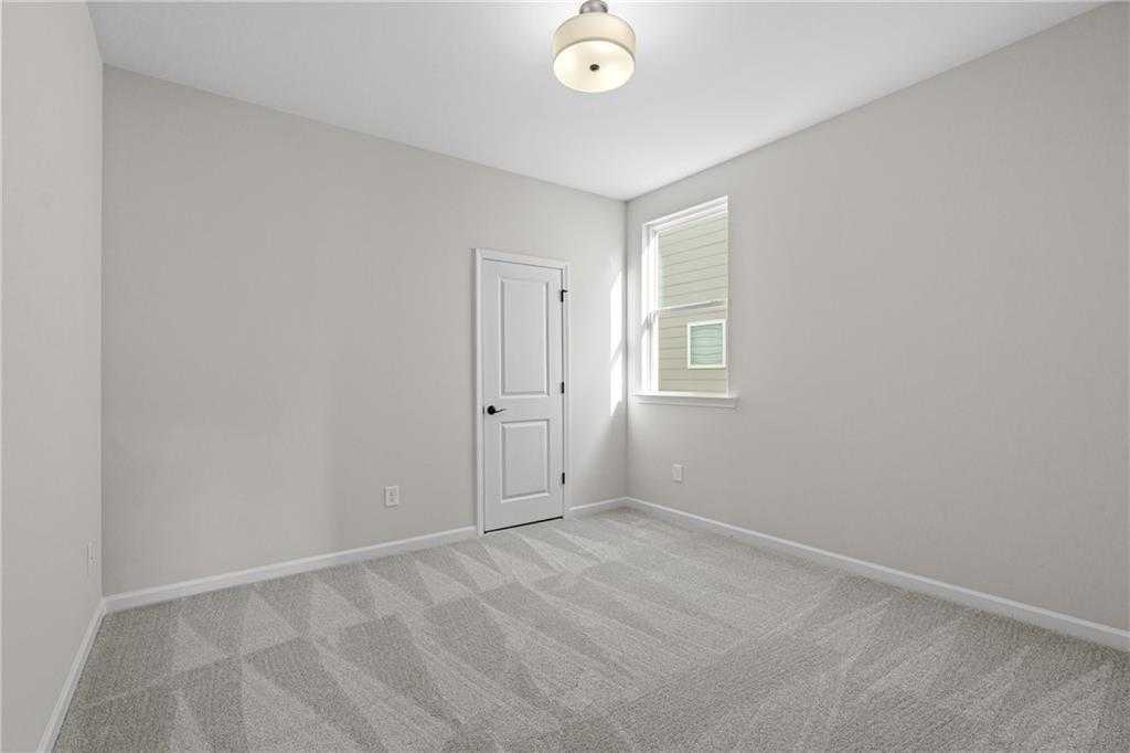 Empty bedroom with neutral gray walls, patterned carpet floor, white door, and window in Davidson Homes The Edison B, Loganville, GA