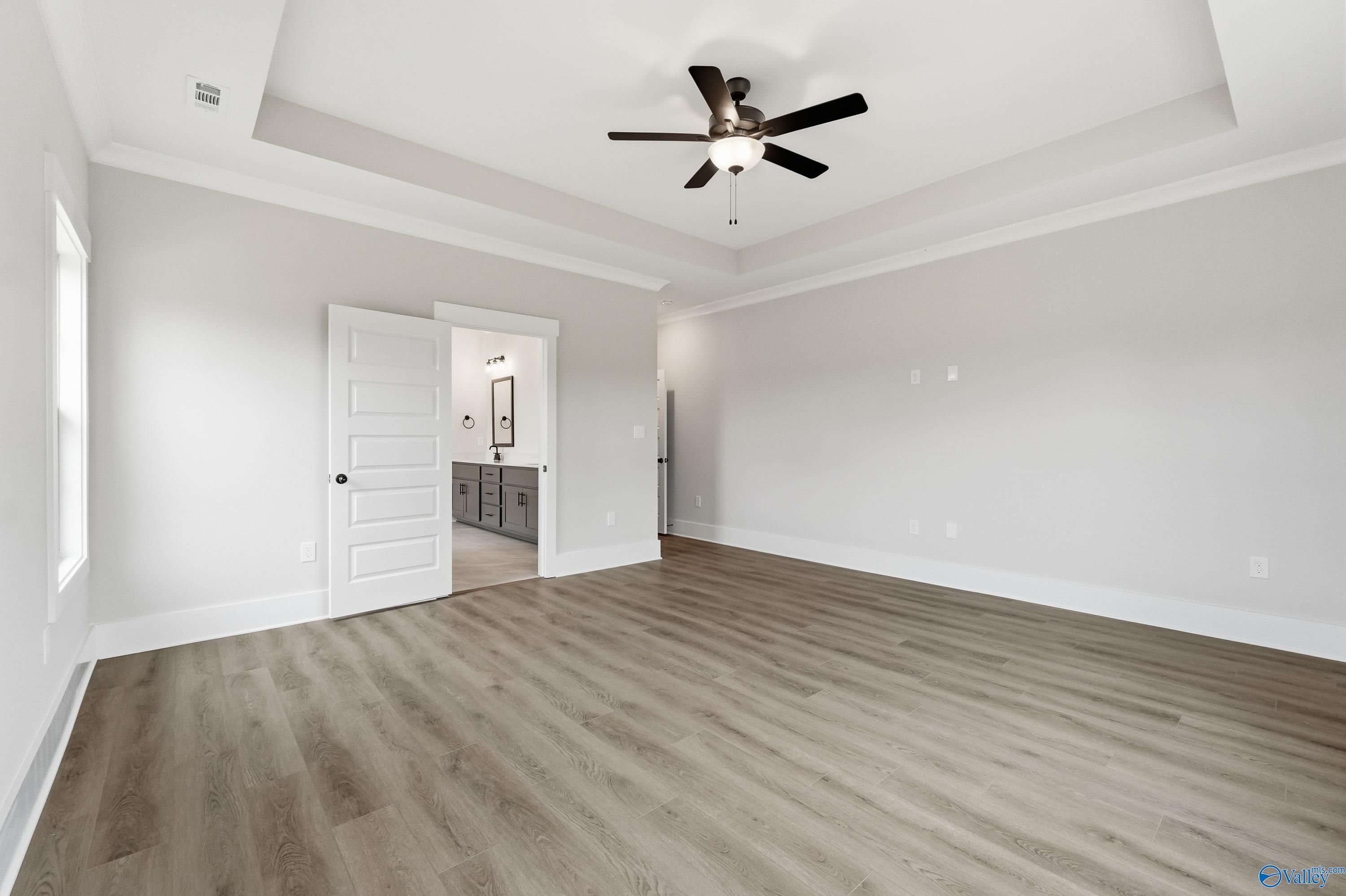 Spacious master bedroom with tray ceiling, black ceiling fan, and open door to bathroom with double vanity in Davidson Homes The Finleigh, Meridianville