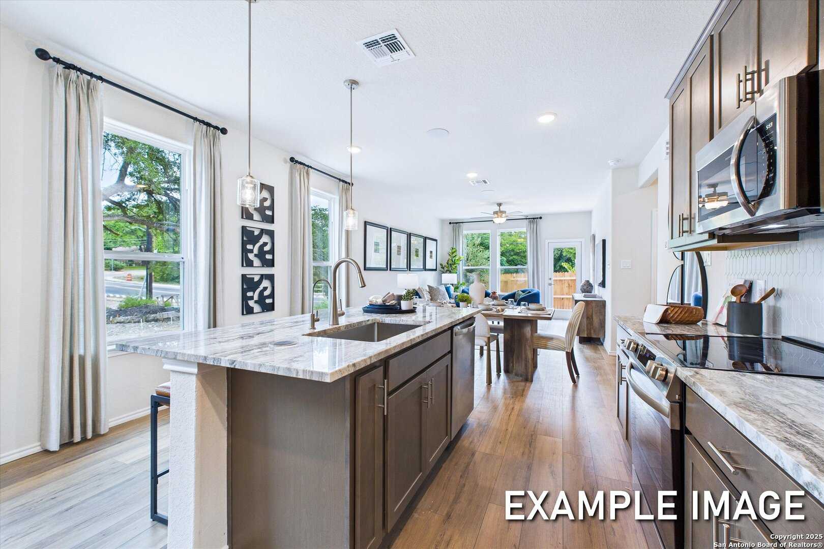 Modern open-concept kitchen with white shaker cabinets, marble island sink, stainless appliances, and adjacent dining in The Gillian C floor plan, San Antonio, Texas