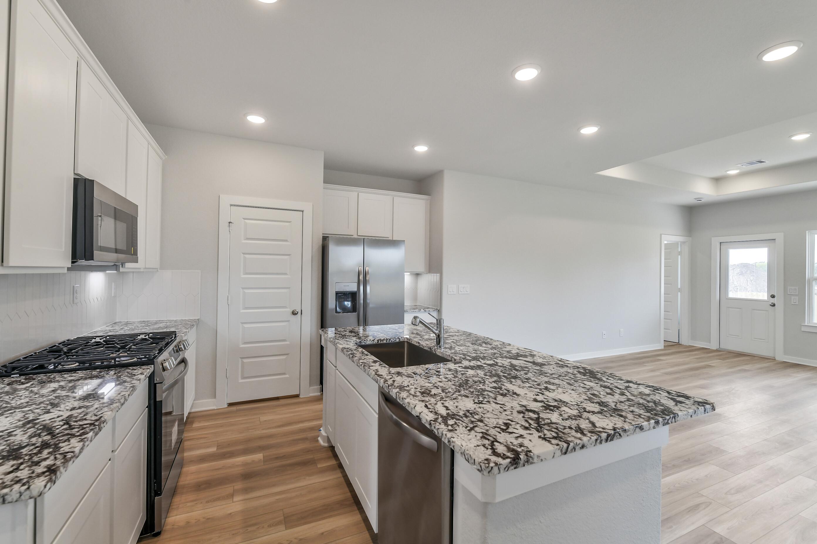Modern kitchen with white shaker cabinets, speckled granite island sink, stainless steel appliances in Davidson Homes The Colorado G, Magnolia TX