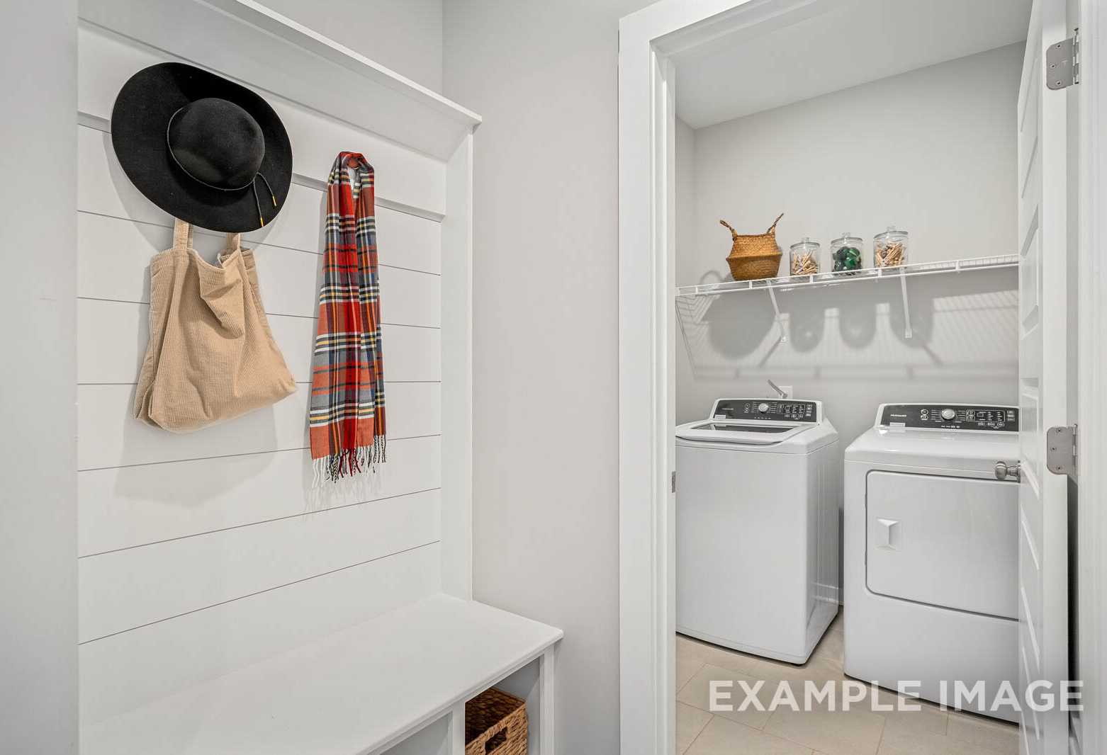 Spacious laundry room in The Franklin C home design with washer, dryer, hanging hooks, and built-in bench