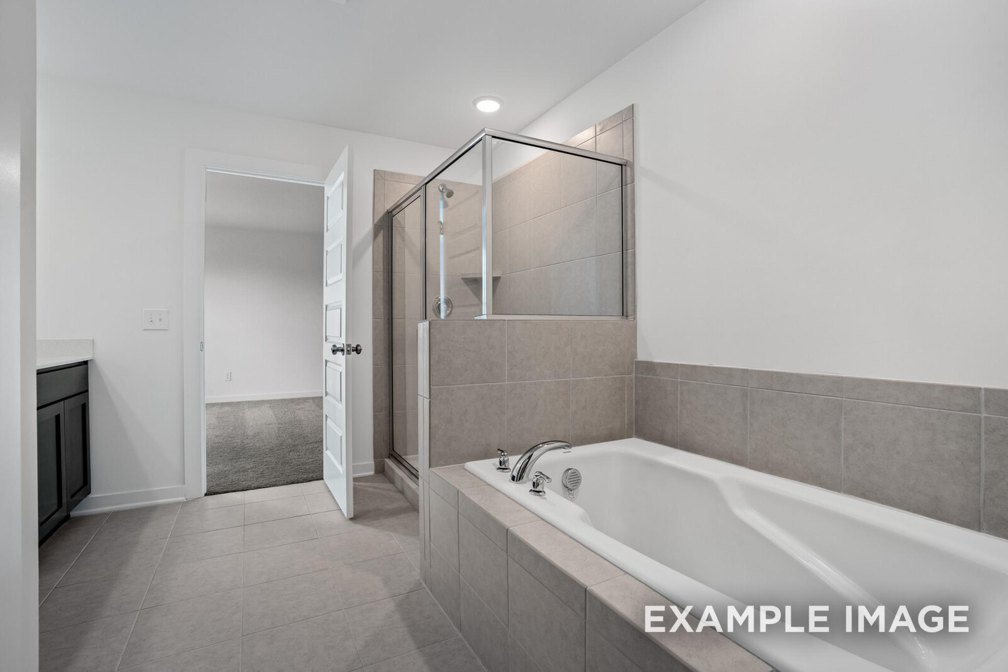 Spacious master bathroom in The Logan C featuring frameless glass shower, soaking tub, and dark vanity