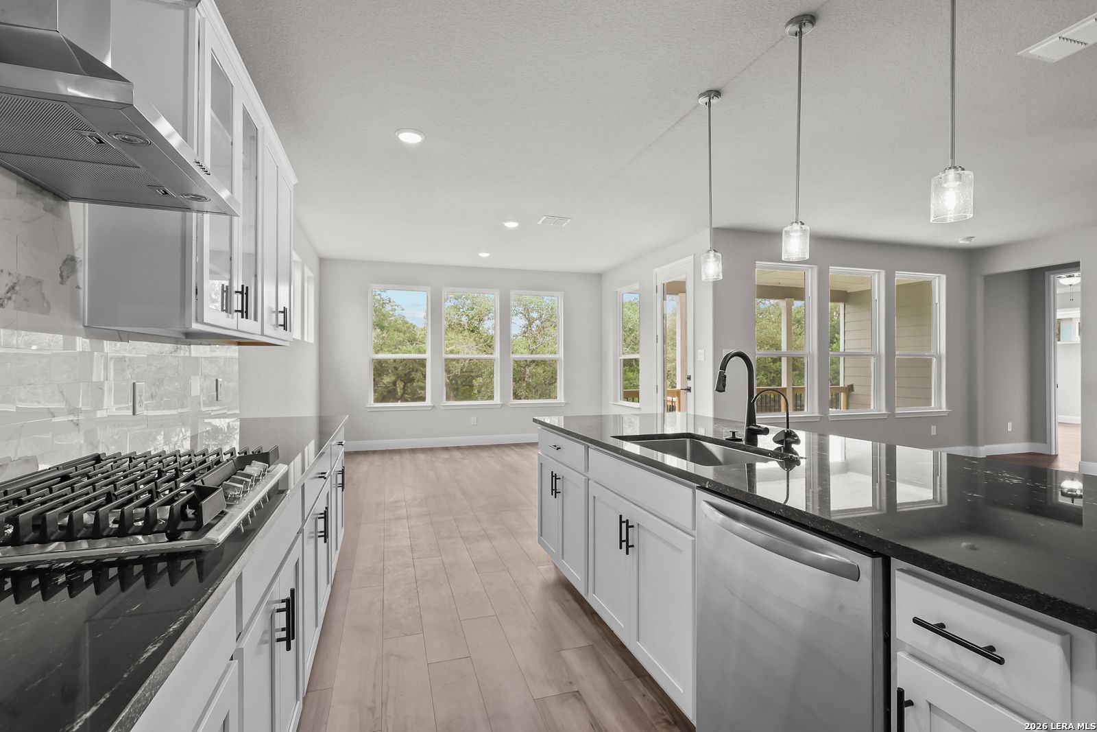 Modern white kitchen with black granite island, gas range, stainless appliances, and large windows in Davidson Homes Belmont H, Castroville TX