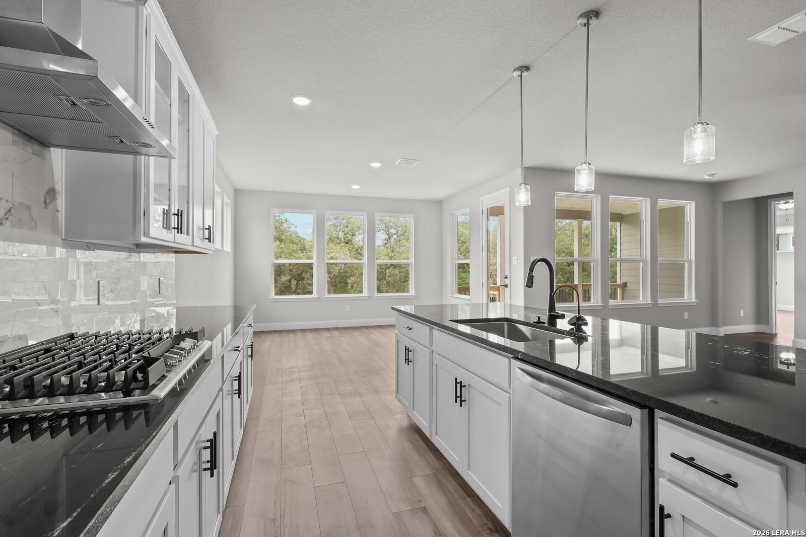 Modern white kitchen with black granite island, gas range, stainless appliances, and large windows in Davidson Homes Belmont H, Castroville TX