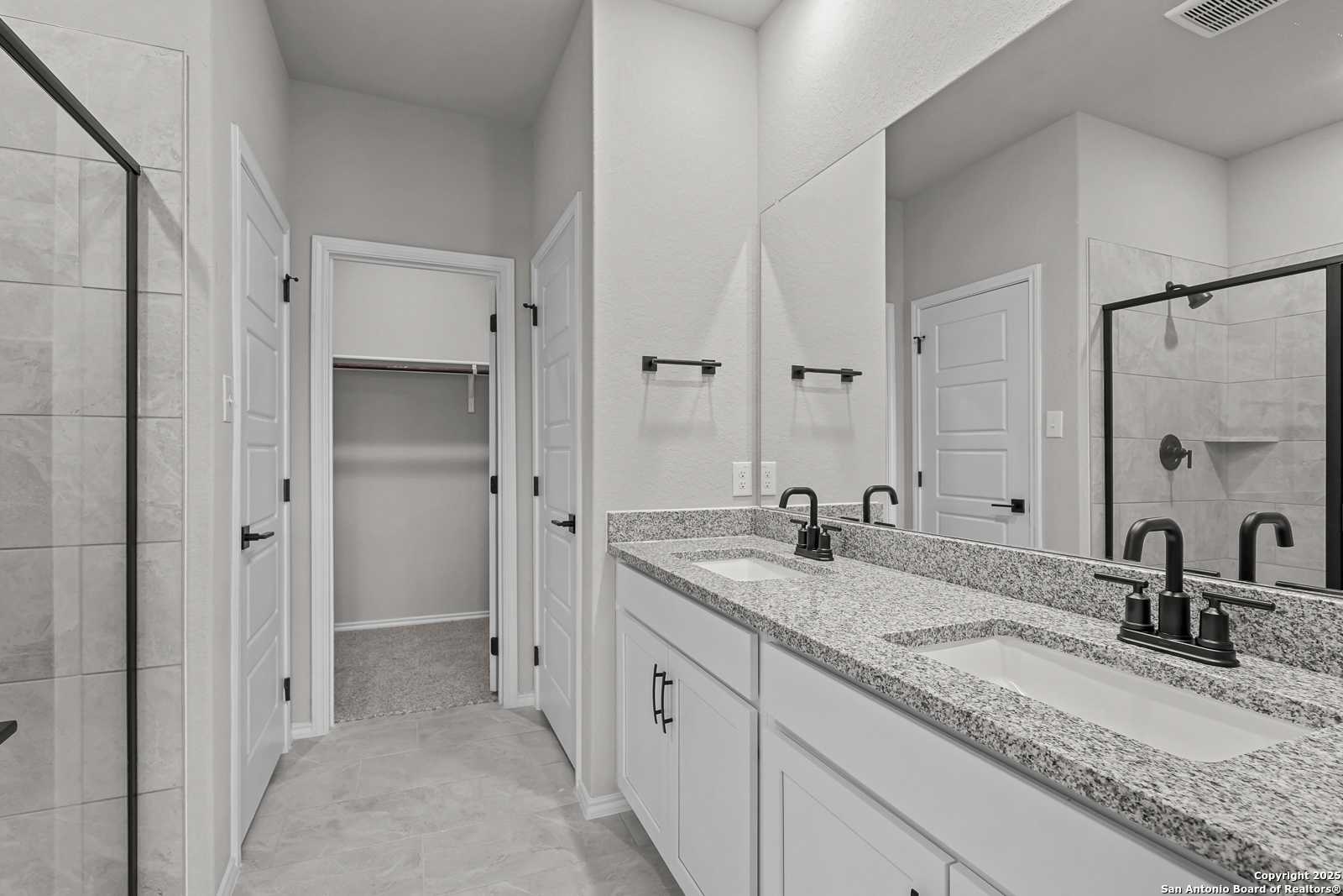 Modern master bathroom featuring double vanity with granite countertop, walk-in shower, and walk-in closet in Davidson Homes The Daphne K, San Antonio