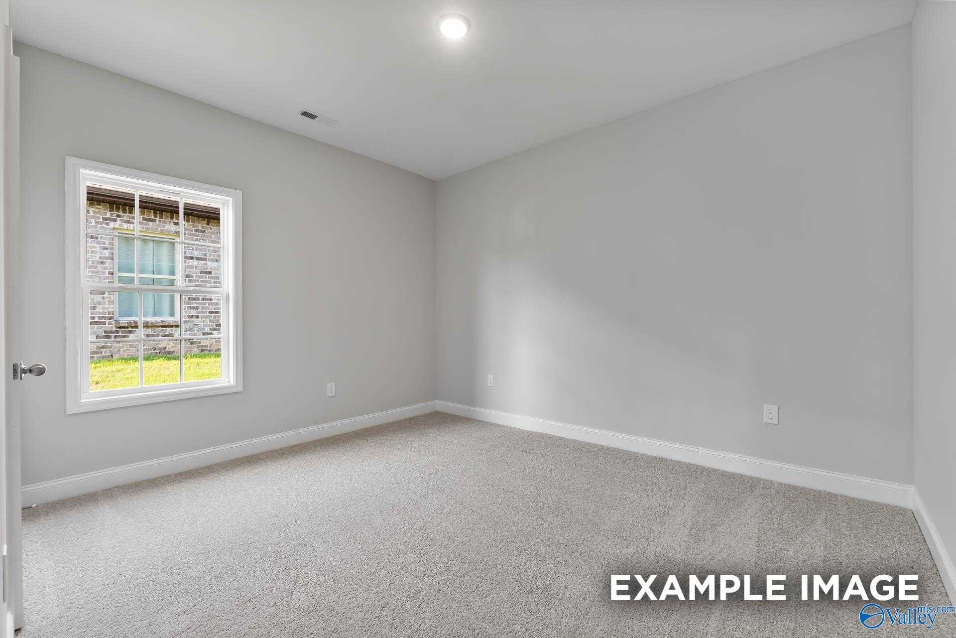 Bright empty bedroom with large window overlooking lawn, neutral gray walls and carpet in Davidson Homes The Daphne C, New Market, AL