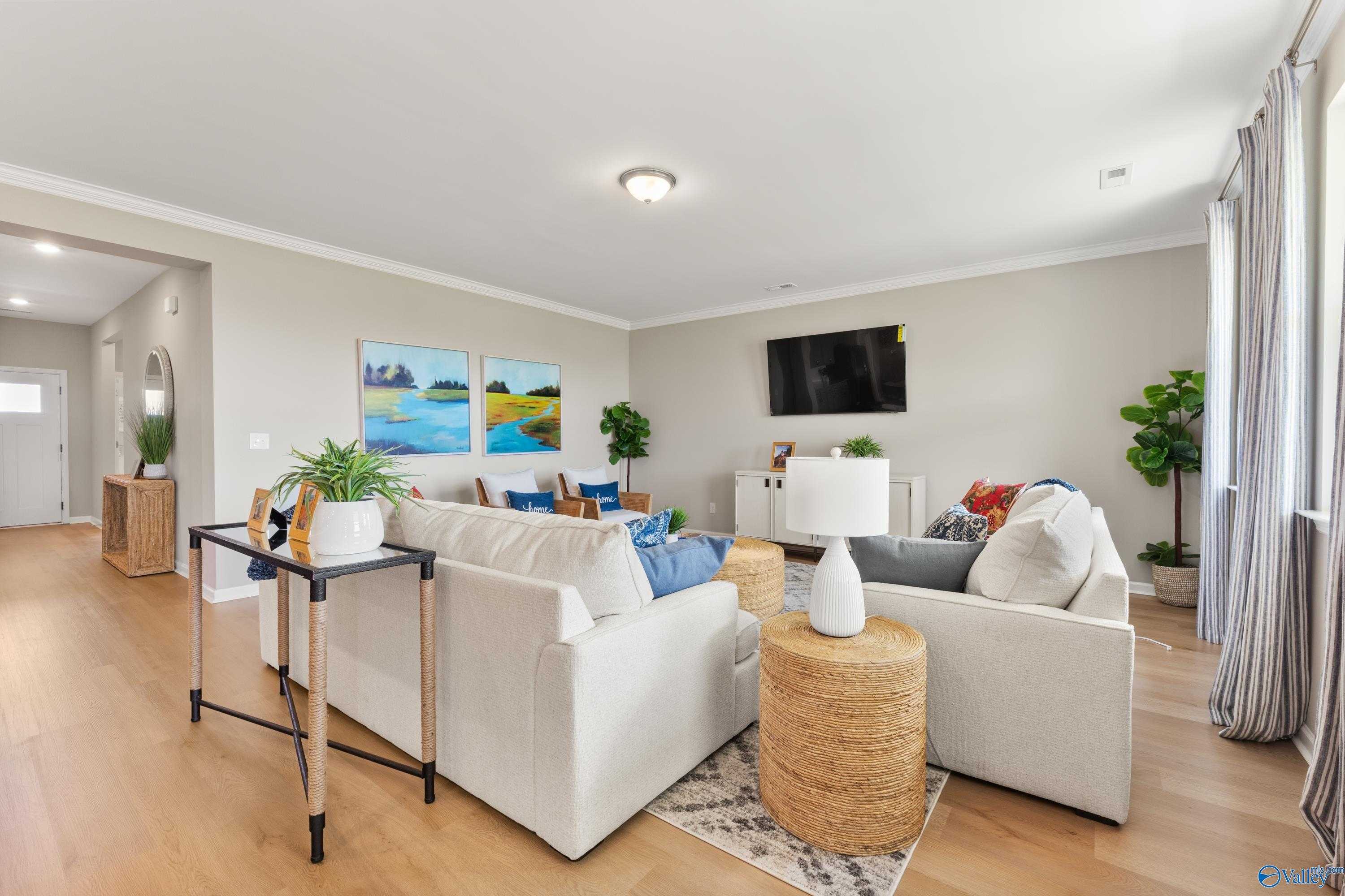 Cozy living room with white sectional sofa, mounted TV, plants, and artwork in Davidson Homes The Sanctuary, Athens Alabama