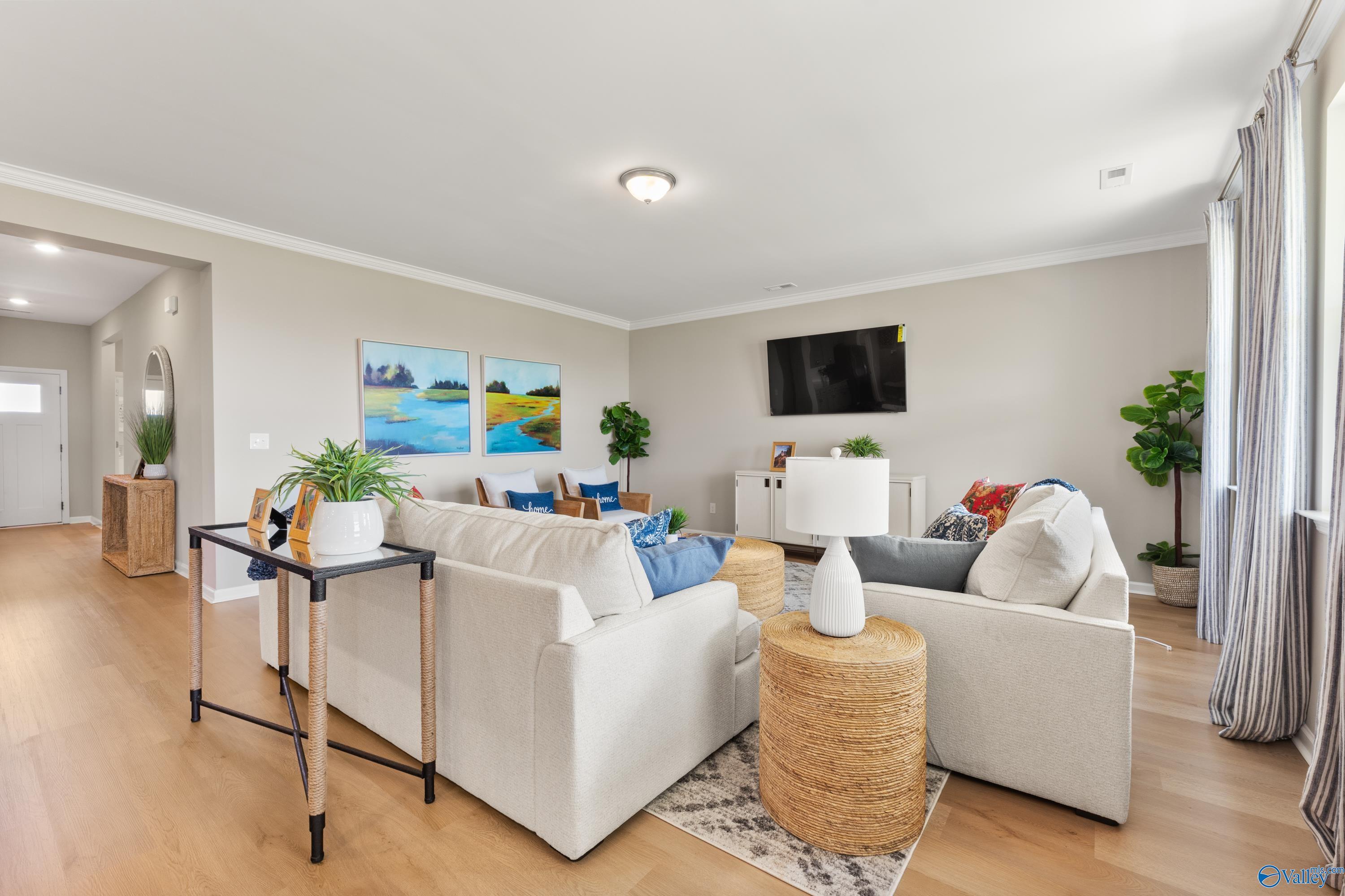 Cozy living room with white sectional sofa, mounted TV, plants, and artwork in Davidson Homes The Sanctuary, Athens Alabama