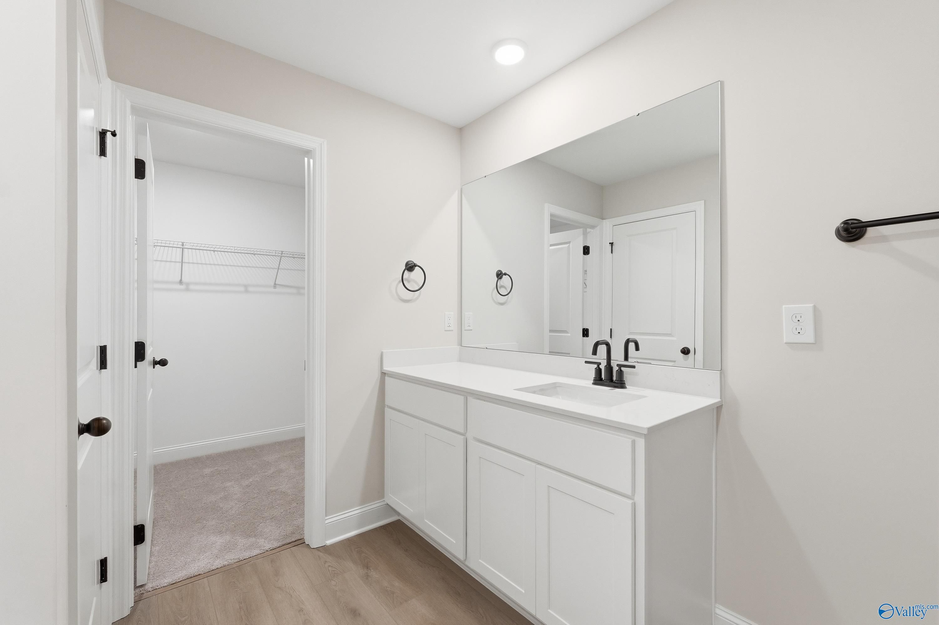 Modern master bathroom featuring white shaker vanity, undermount sink, large frameless mirror, and open walk-in closet in Davidson Homes The Franklin V, Athens, Alabama