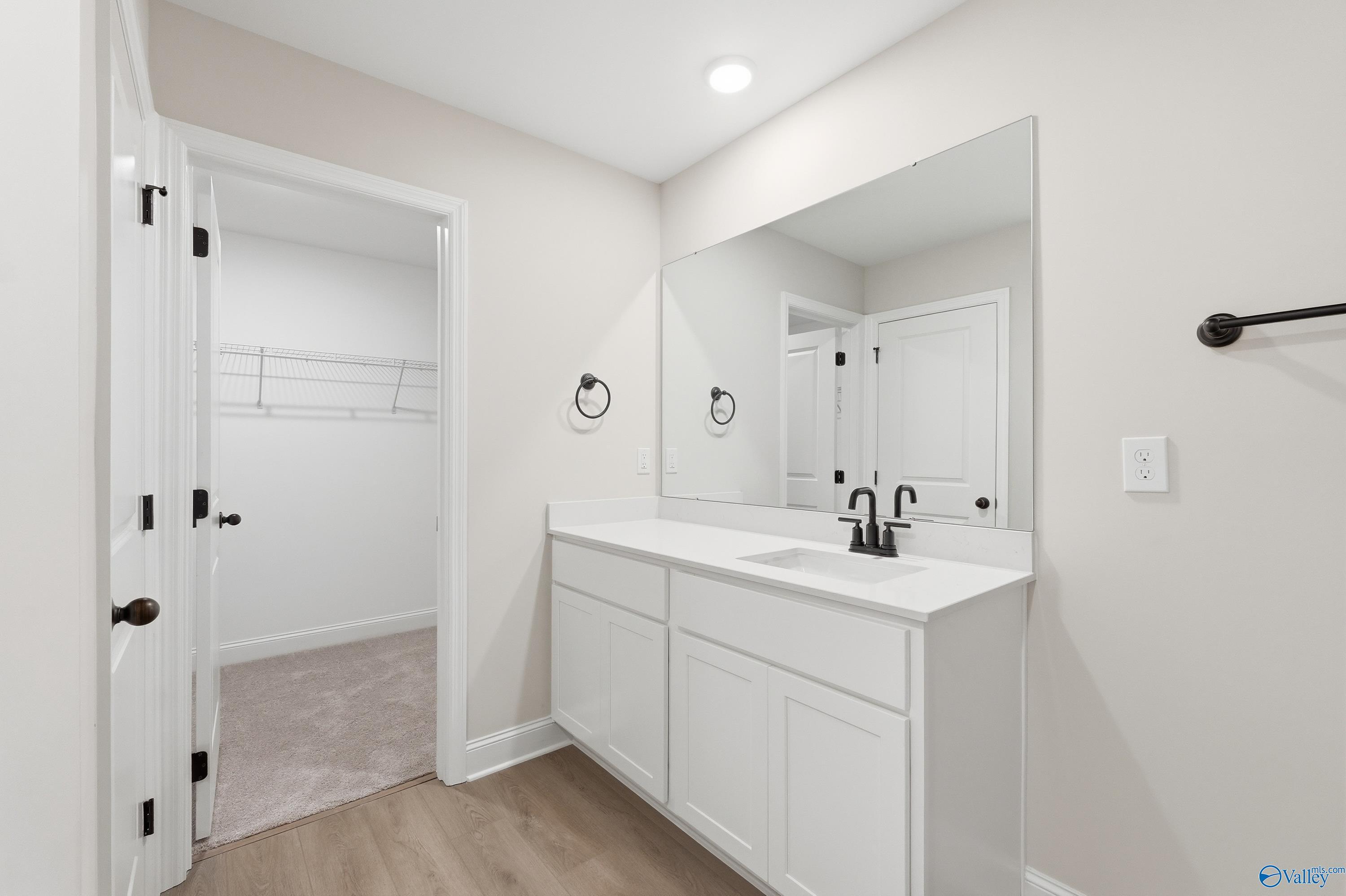 Modern master bathroom featuring white shaker vanity, undermount sink, large frameless mirror, and open walk-in closet in Davidson Homes The Franklin V, Athens, Alabama