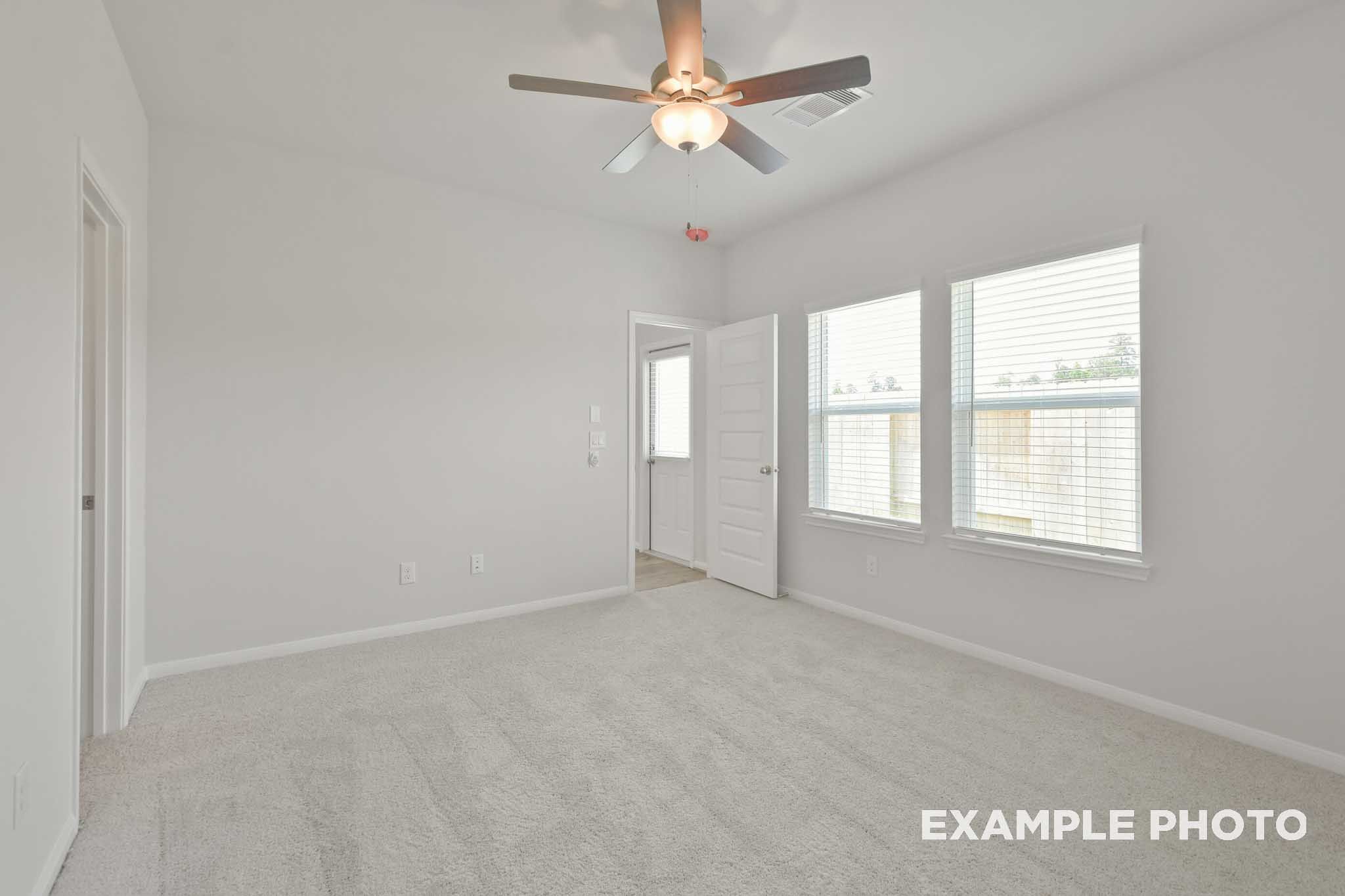 Spacious master bedroom in The Comal by Davidson Homes featuring ceiling fan, neutral gray walls, beige carpet, and large windows in Magnolia Texas