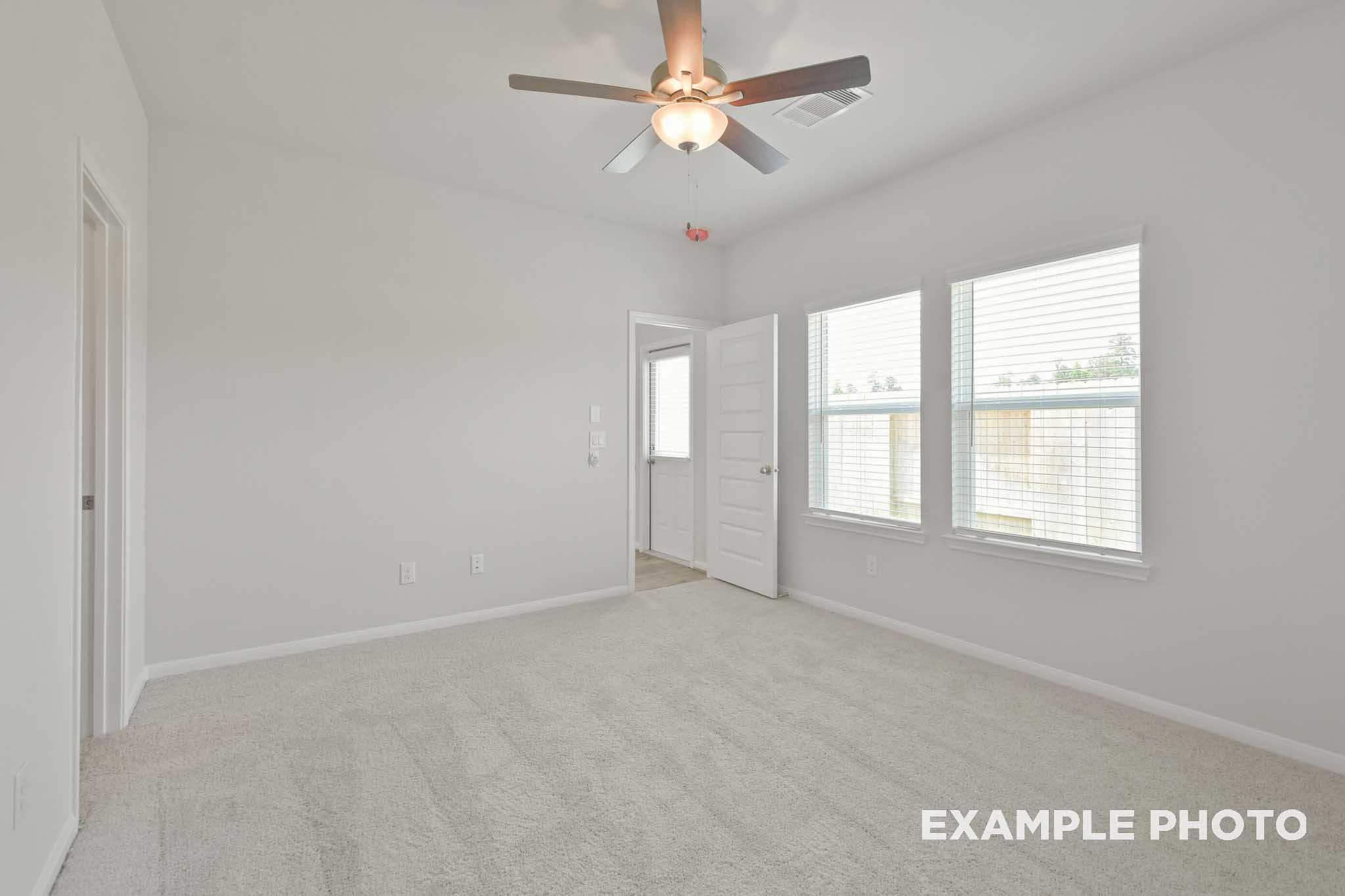 Spacious master bedroom in The Comal by Davidson Homes featuring ceiling fan, neutral gray walls, beige carpet, and large windows in Magnolia Texas