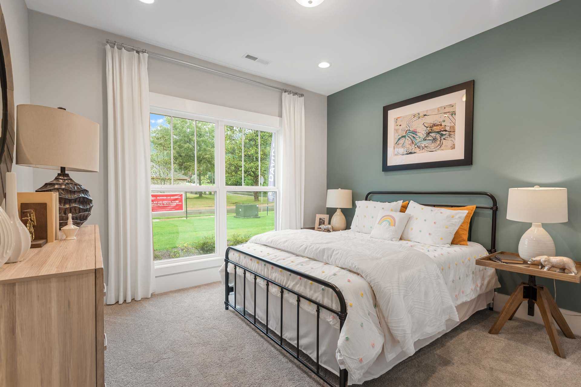Serene bedroom at Monteagle Cove in Owens Cross Roads, Alabama with sage green walls, large window overlooking lawn, and metal bed with white bedding
