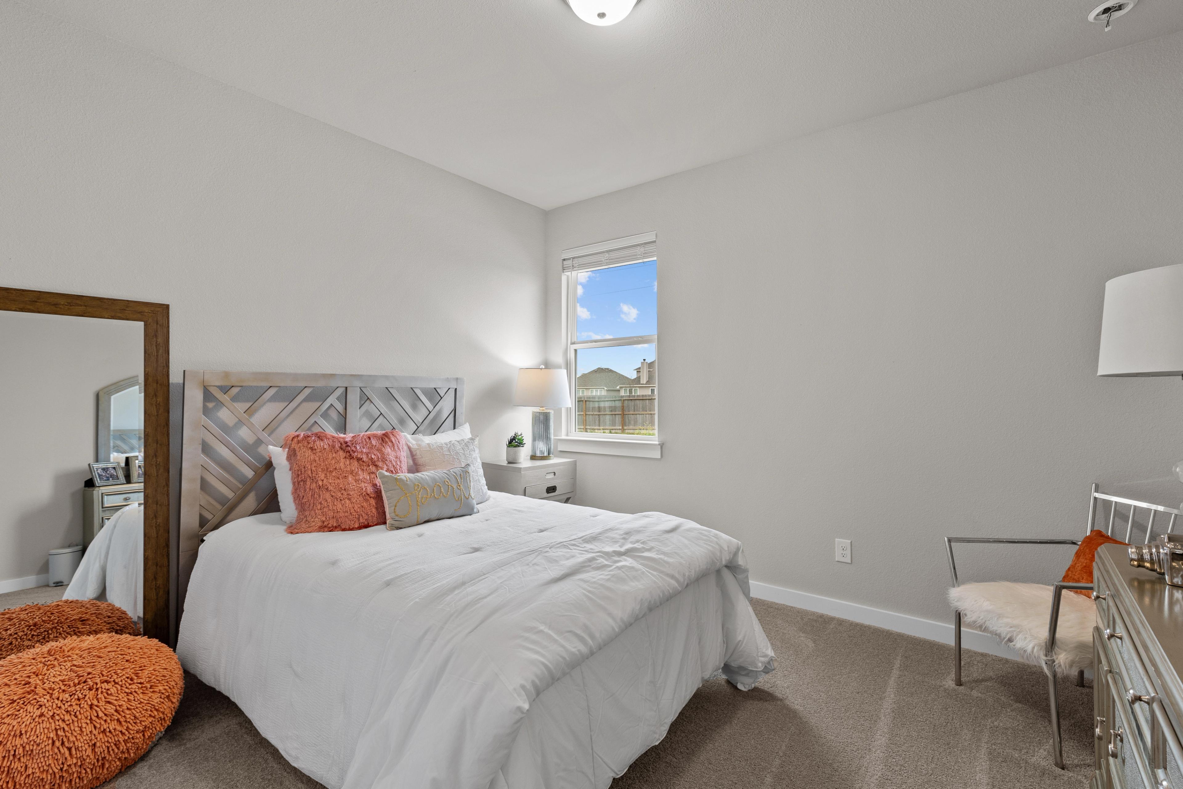 Bright bedroom interior at Hannah Heights in Seguin Texas by Davidson Homes with white bedding orange accents gray walls and window view