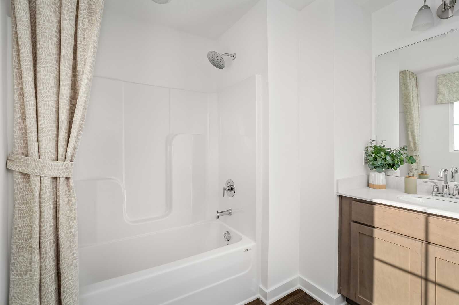 Modern bathroom with white tub, shower combo, beige curtains, and wooden vanity in The Cumberland A Interior, Gallatin, TN