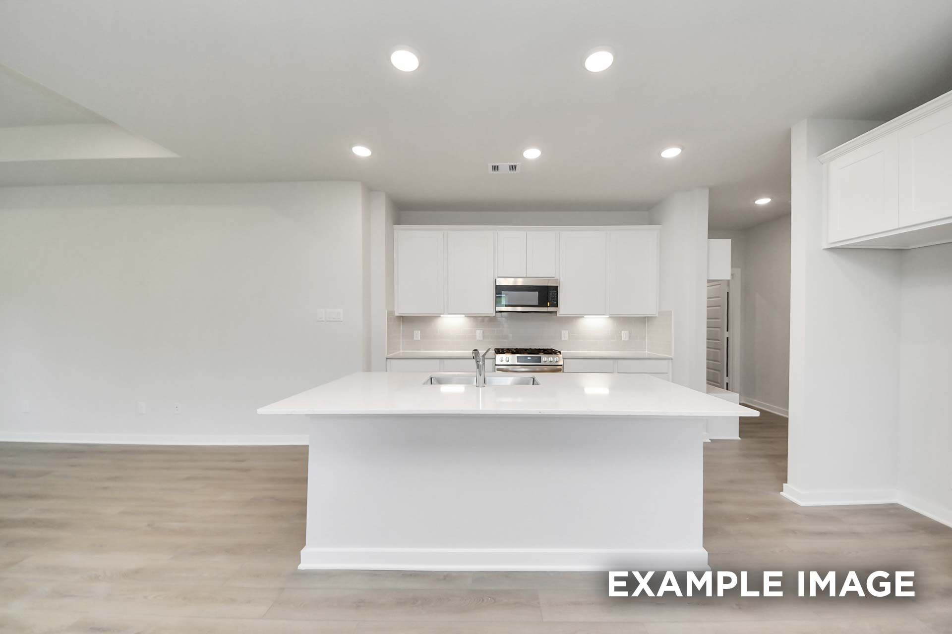 Bright open-concept kitchen with large white island and sink in The Blanco by Davidson Homes, Beasley, Texas