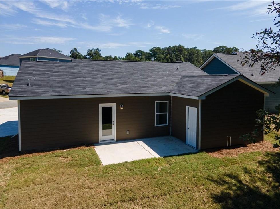 Rear view of single-story brown-sided home with shingle roof, glass door, and concrete patio in Summer Vineyard, Phenix City, Alabama