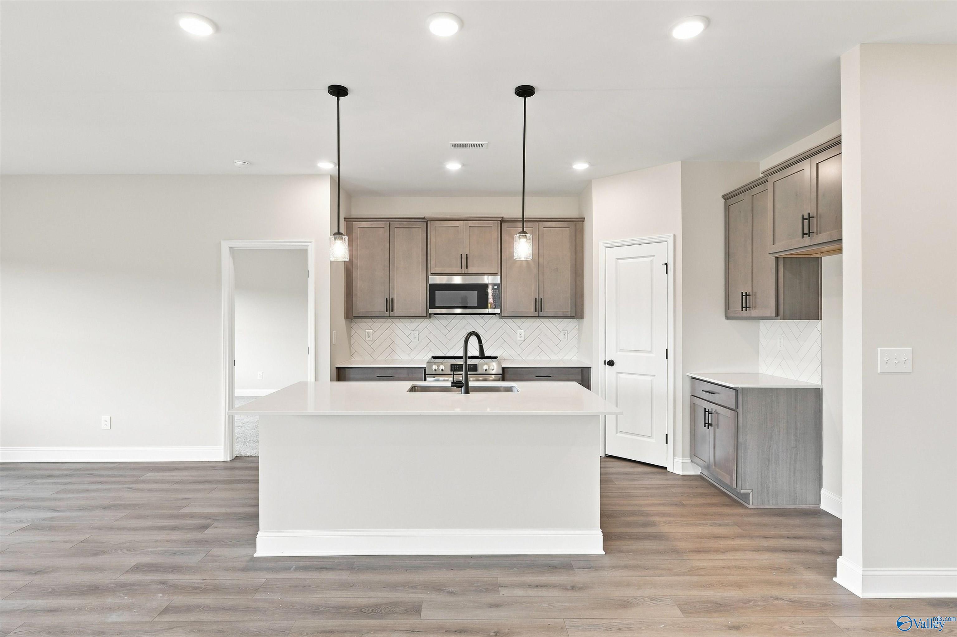 Modern kitchen island with pendant lights, herringbone backsplash, and gray cabinetry in Davidson Homes Franklin C plan, Athens AL