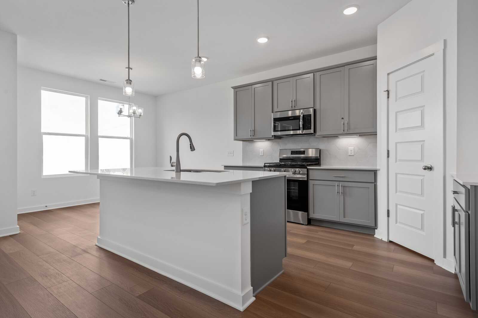 Spacious modern kitchen in The Asheville with white quartz island, gray cabinets, stainless appliances, pendant lights, hardwood floors