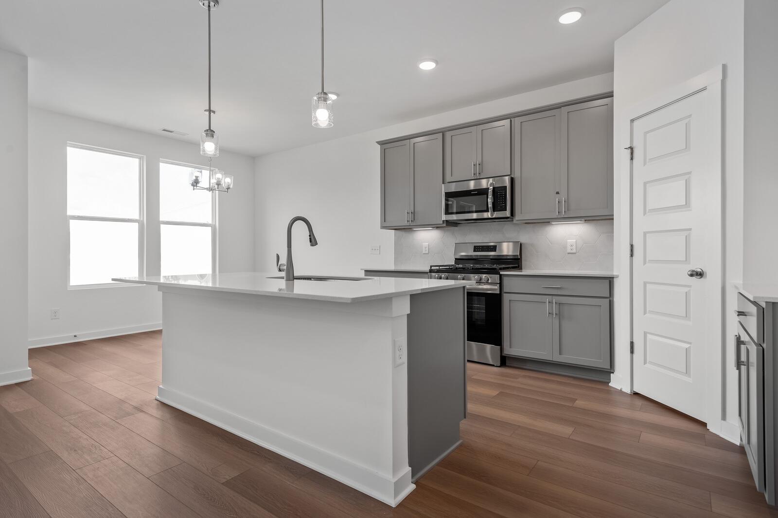 Spacious modern kitchen in The Asheville by Davidson Homes: white quartz island, gray cabinets, stainless appliances, hardwood floors