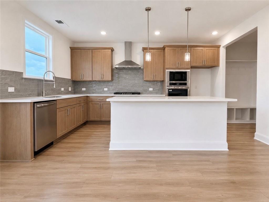 Modern kitchen with white island, stainless appliances, and wood cabinets in The Hickory C plan, Wehunt Meadows, Hoschton.