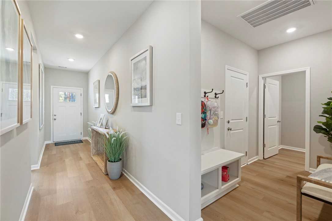 Bright entryway hallway with oak hardwood floors, coat hooks, round mirror, and potted plant in Davidson Homes Phoenix B, Opelika AL