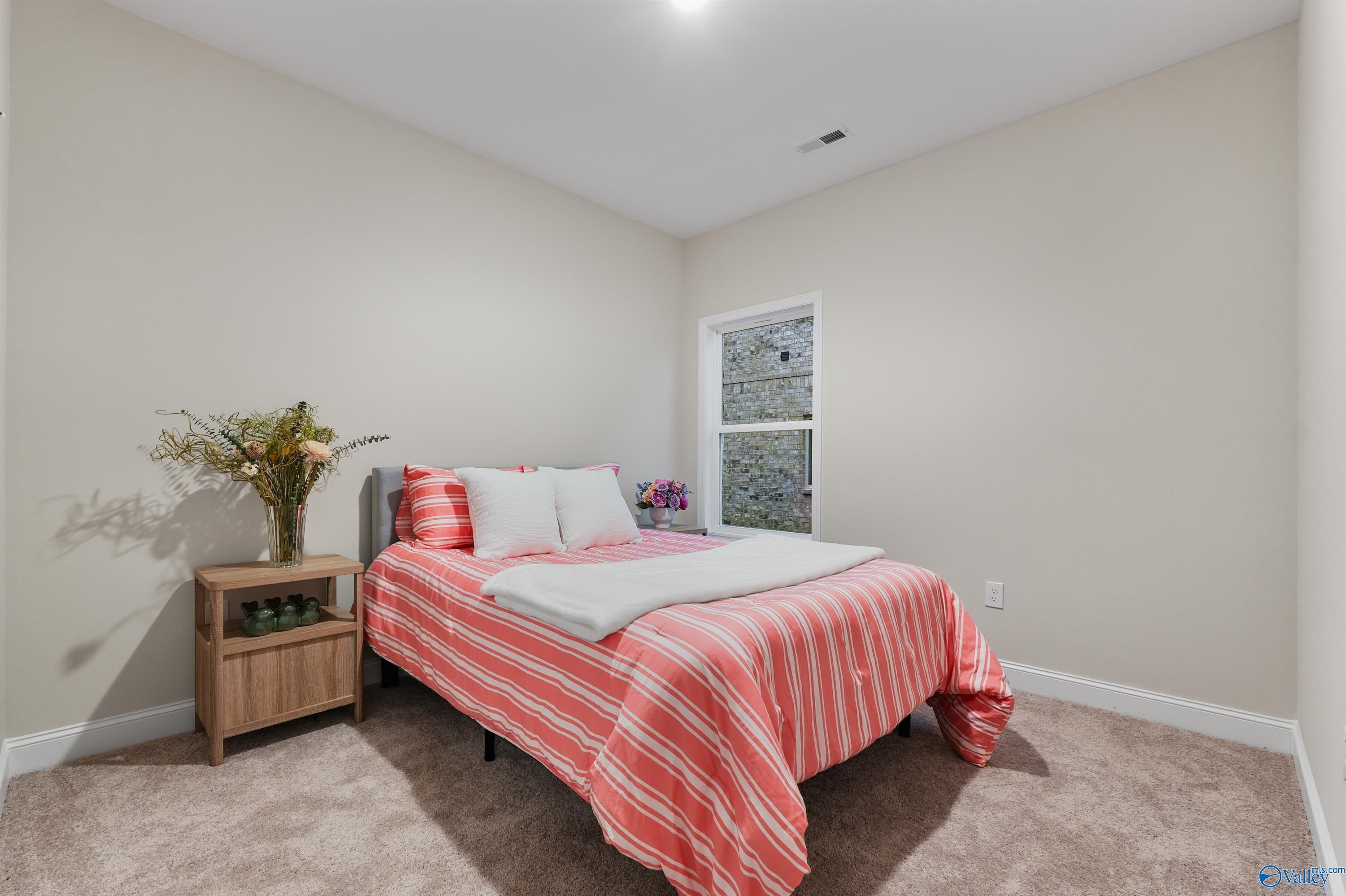 Cozy secondary bedroom with pink striped bedding, floral vase on nightstand, neutral walls in The Asheville C, Jaguar Hills, Huntsville AL