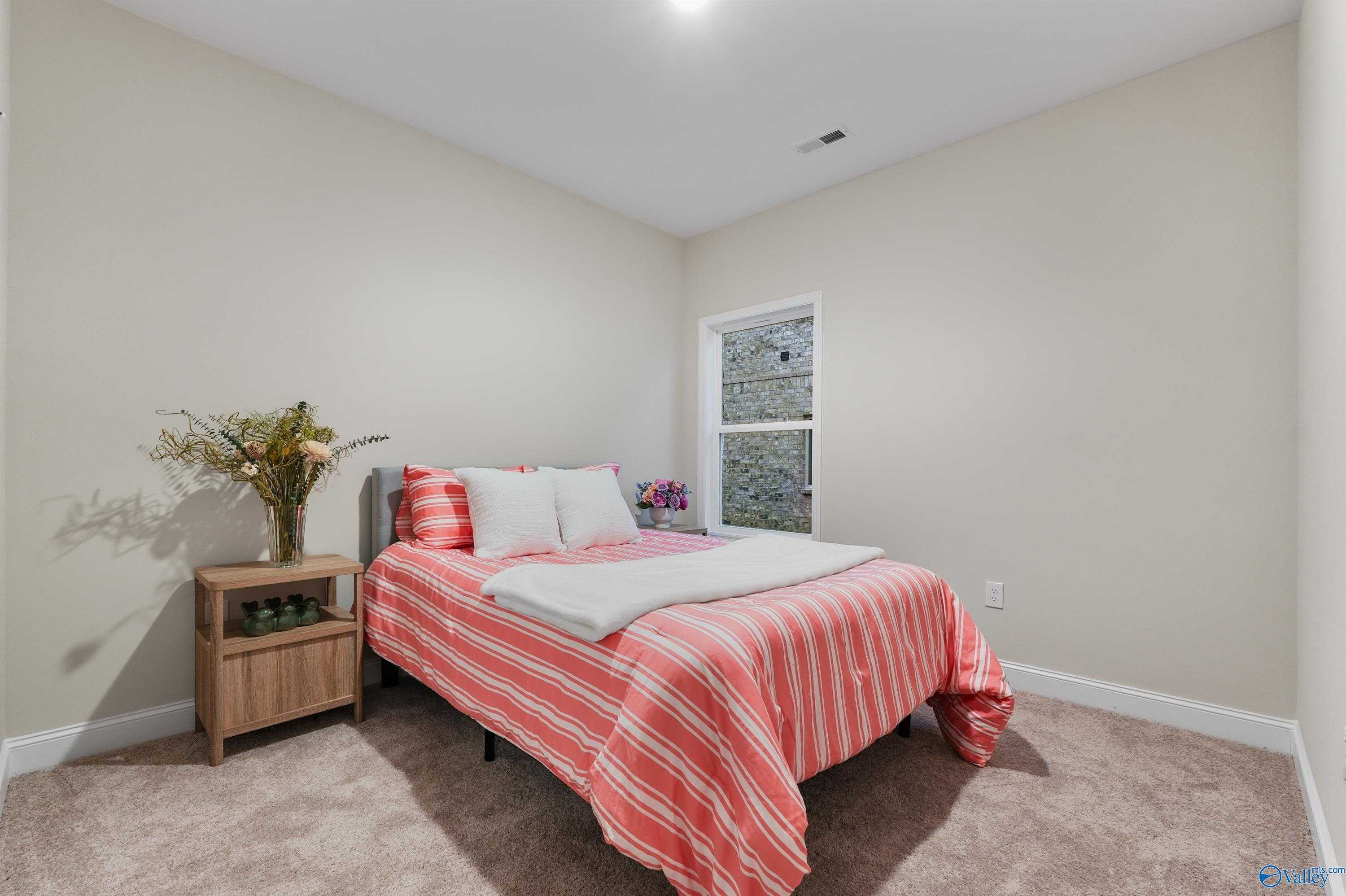 Cozy secondary bedroom with pink striped bedding, floral vase on nightstand, and neutral walls in Davidson Homes The Asheville C, Huntsville, AL